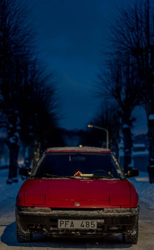 Snöig röd gammal mazda i en trädallé